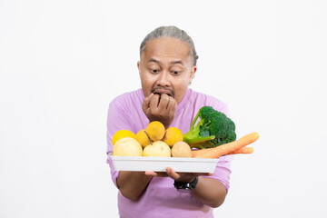 curly-haired Asian adult male carrying a tray of fresh vegetables while pointing at it, healthy and nutritious fresh vegetables eating campaign, healthy lifestyle