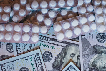 White pills in blister packs and dollar bills close-up, cost of treatment, expensive medications, pharmaceutical business.