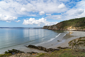 La plage de Trez Bihan, à marée basse, dévoile son sable doré, entourée de falaises imposantes sous un ciel bleu parsemé de nuages blancs. Un paysage typique de la baie de Douarnenez en Bretagne.