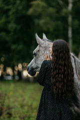 The girl is stroking the horses. A girl and horses in nature. Horses in nature in summer with a girl.