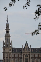 Fototapeta premium Historic Tower and Facade of Antwerp Building Framed by Leaves with Crane in Background 