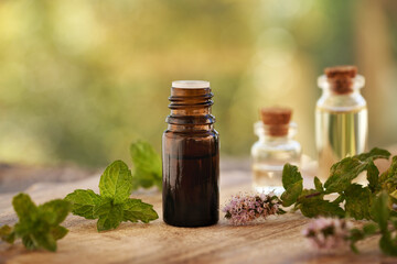 A brown bottle of aromatherapy essential oil with fresh peppermint leaves and flowers