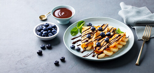 Crepes, thin pancakes with chocolate sauce and fresh blueberries. Grey background. Close up.