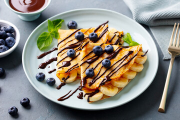 Crepes, thin pancakes with chocolate sauce and fresh blueberries. Grey background. Closeup.