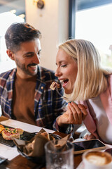 Couple feeding eachother in a restaurant with delicious food.