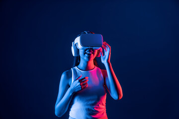 Smart female stand in cyberpunk neon light wearing VR headset connecting metaverse, futuristic cyberspace community technology. Elegant woman excited seeing generated virtual scenery. Hallucination.