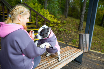 A woman on a walk with a dog. A dog in a fashionable jacket and glasses, training