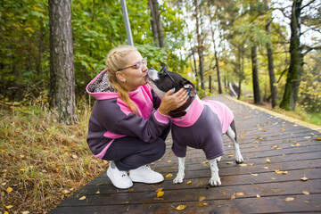 an adult woman in a tracksuit on a walk with a dog. A dog in a fashionable sweater and glasses