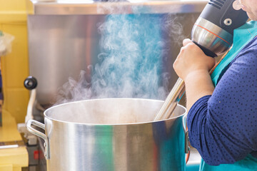 Chef is using an immersion blender in a large pot while preparing food in a professional kitchen. Selective focus