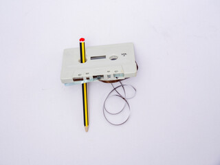 Plastic retro cassette with loose magnetic tape being wound by a pencil on a white background