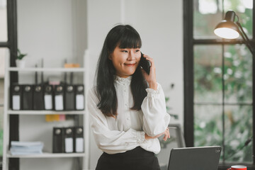 Businesswoman is standing in her office smiling while talking on her cell phone and working on a project