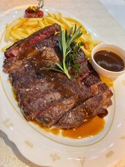 Grilled rib-eye cooking a medium-rare steak with fried potato and sauce in saucer over table.