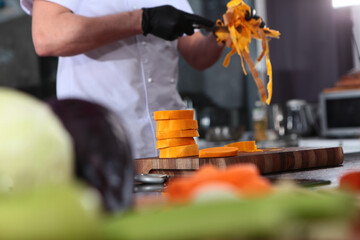 Pieces of pumpkin are lying on a wooden board. The cook peeled the pumpkin. The cook's hands are out of focus. We prepare the ingredients for a seasonal autumn dish, soup or pie.
