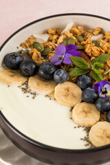 A healthy nutritious breakfast of natural Greek yoghurts, granola and fresh berries on pink background.