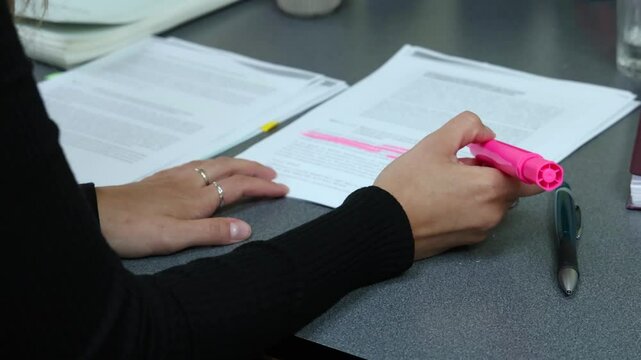 Woman highlights text on a document with a pink highlighter in slow motion, showcasing focus and concentration. Selective focus