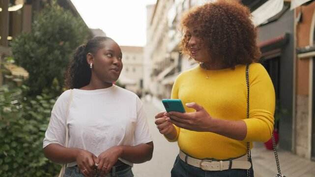Gen z female friends talking and walking while using cellphone in the street. Natural conversation.