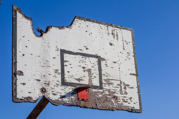 Damaged wooden basketball backboard without a hoop against blue sky