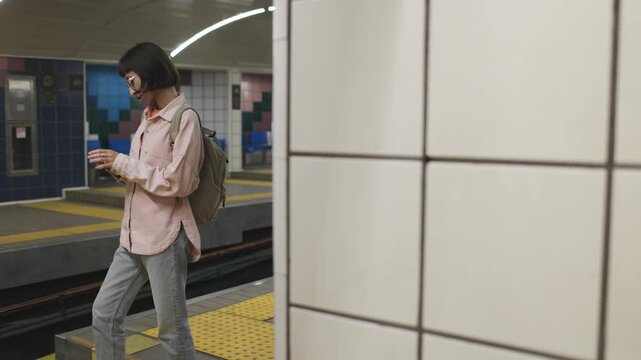 young woman stands at a metro station and looks at her mobile phone. a woman uses a mobile phone at a metro station. the girl looks at the schedule.