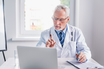 Obraz premium Senior doctor on video chat with patient at hospital. Online conference and meeting. Telemedicine