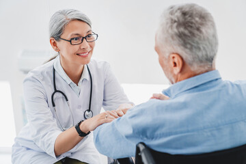Adult female doctor talking to senior patient in wheelchair at hospital. Support concept