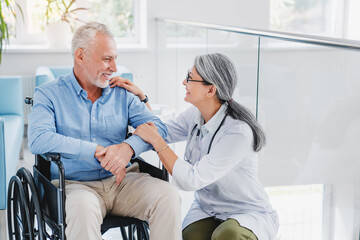 Smiling female doctor physiotherapist taking care of happy senior patient in wheelchair