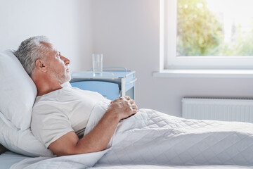 Side view of thoughtful senior male patient in hospital bed in ward room