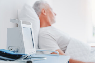 Fototapeta premium Close up of medical monitor with senior male patient in ward at hospital