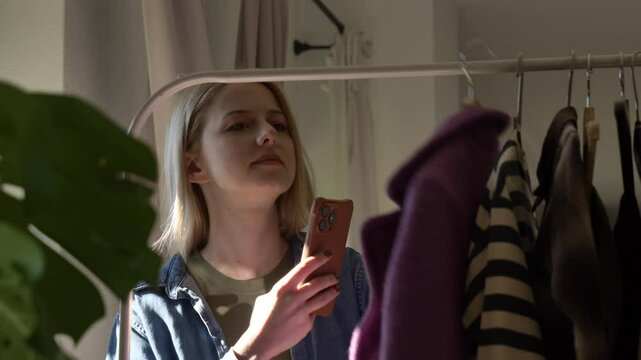 European woman selecting clothes from her wardrobe at home and photographing them for online sale, video