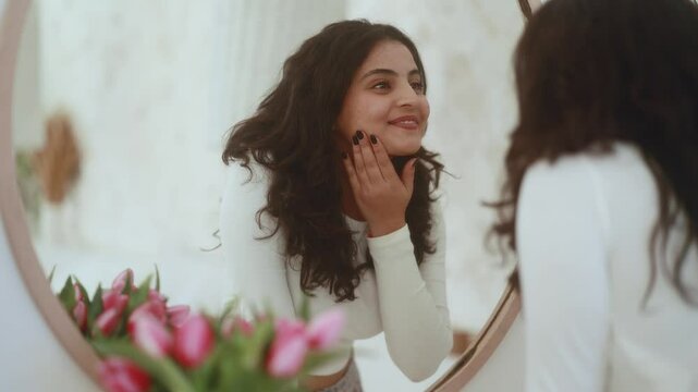 Portrait of pretty young indian woman touching facial skin check quality of care products while looking at mirror reflection at home Healthy skin care treatment beauty concept