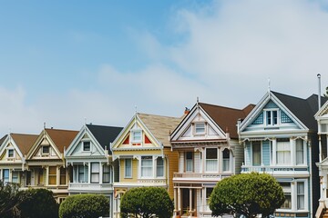 Victorian-style colorful houses in a row, showcasing historic architecture and charm in a peaceful, tree-lined neighborhood under a bright sky