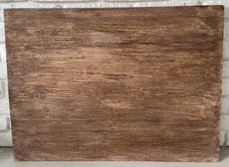 Rustic wooden panel leans gracefully against a textured white brick wall, showcasing its rich grain patterns and natural warmth. Contrast between the organic wood and the structured brick provides a