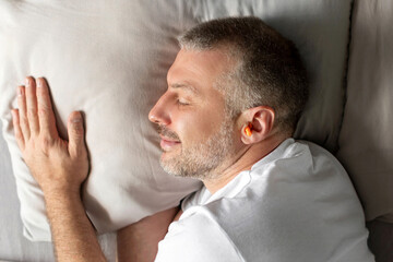  A middle-aged European man sleeping on a bed with orange earplugs in his ear will give you peace...