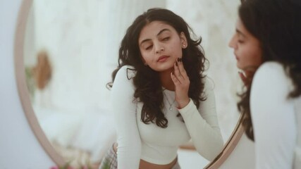 Portrait of pretty young indian woman touching facial skin check quality of care products while looking at mirror reflection at home Healthy skin care treatment beauty concept