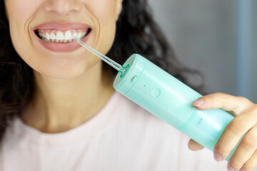Woman using oral water irrigator, cleaning teeth with modern equipment, closeup. Dental oral care concept