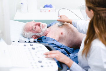 Close up photo of mature male patient undergoing ultrasound examination with female doctor in the foreground