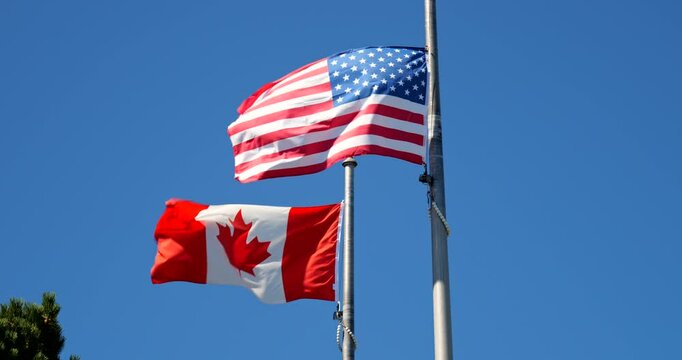 Canadian and American flags wave side by side at the country border, symbolizing international friendship and cooperation amid a windy backdrop