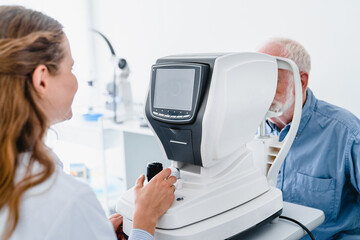 Woman doctor examining elderly man`s eyes by using special ophthalmic apparatus