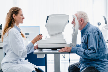 Woman oculist examining old man`s sight with ophthalmic tool