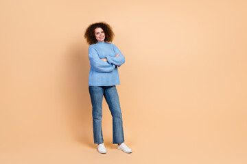 Full body photo of young confident beautiful curly haired lady in blue knitted sweater folded hands isolated on beige color background