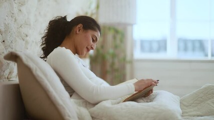 Relaxed young indian woman reading book literature laying on bed at cozy home Calm relaxed smiling female enjoying weekend leisure time alone indoors