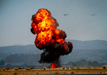 A dramatic explosion of military munitions with a ball of orange fire and jets flying in the...