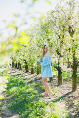 A young woman in a light blue dress in a blooming garden. A cute woman on a walk in the garden.