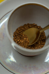 A spoonful of coffee in a mug on a saucer on a yellow background. Close up