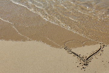 heart in the sand being washed away by a wave, symbolic beach photo for grief, romance, or loss.