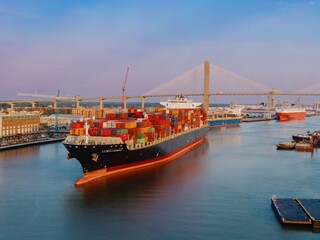 Cargoship on the Savannah River at sunrise. Alongside is the waterfront of the North Historic...
