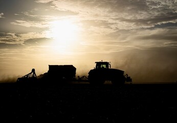 Fototapeta premium tractor sowing seeds black silhouette at sunset