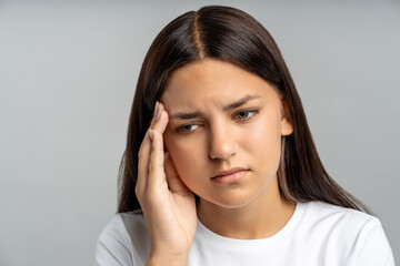 Distressed teen girl covers face, nearly in tears against grey wall. Overwhelmed by school stress, sleepless nights, emotional trauma from bullying, abuse, feeling trapped, ashamed, deeply isolated