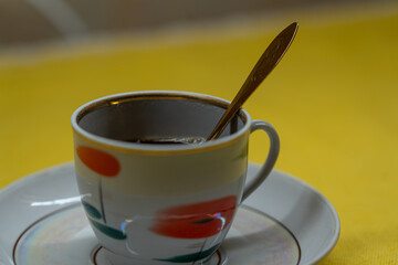 A golden spoon in a coffee mug. A mug in a saucer on a yellow background