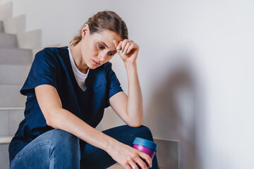 Tired female medical worker doctor holding cup of coffee taking pause in work