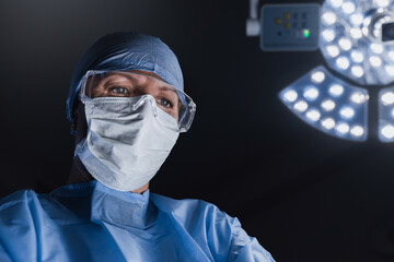 Doctor performing surgery in dark operation room with lamp on background